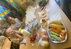 Dziewczynki siedzą przy stole pełnym owoców, jogurtów i warzyw