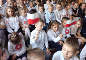Uczniowie klas 0-III w galowych strojach z polskimi flagami i kotylionami