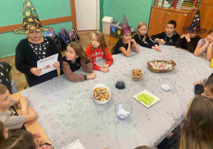 Dzieci siedzą przy stole, jedna z uczennic w kapeluszu czarownicy czyta wróżby