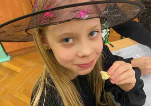 Dziewczynka w kapeluszu czarownicy je ciasteczko