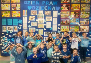 Dzieci klas 1-3 ubrane na niebiesko, pozujące do zdjęcia na tle tablicy samorządu z umieszczonymi informacjami o Prawach Dziecka.