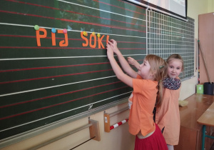 Dziewczynki wieszają na tablicy ułożony napis.