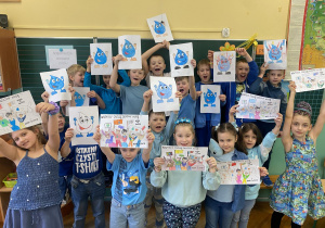 zdjęcie przedstawia uczniów klasy pierwszej, ubranych na niebiesko, trzymających w rękach narysowane kropelki wody oraz plakaty dotyczące oszczędzania wody.