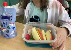 Zdjęcie przedstawia uczennicę podczas drugiego śniadania, w śniadaniówkach ma kolorowe owoce i warzywa oraz smaczne musy owocowe