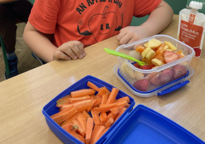 Zdjęcie przedstawia ucznia podczas drugiego śniadania, w śniadaniówkach ma kolorowe owoce i warzywa oraz smaczne musy owocowe