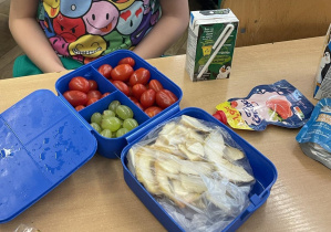 Zdjęcie przedstawia ucznia podczas drugiego śniadania, w śniadaniówkach ma kolorowe owoce i warzywa oraz smaczne musy owocowe